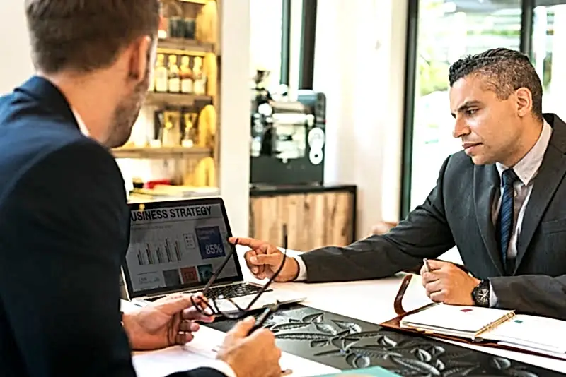 İki iş insanının veya avukatın bir araya gelerek laptop ekranındaki iş stratejilerini incelediği, iş hukuku danışmanlığını temsil eden görsel.