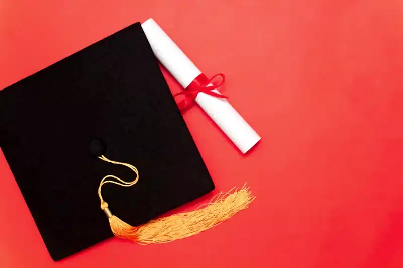 Kırmızı zemin üzerinde mezuniyet kepi ve diploma – doçentlik unvanı iptali, etik ihlal ve sahtecilik süreçleri.