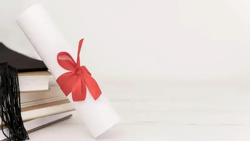 Beyaz bir arka plan üzerinde, kırmızı kurdeleyle bağlanmış bir diploma rulosu, yanında istiflenmiş kitaplar ve bir mezuniyet kepiyle akademik başarıyı temsil eden görsel.