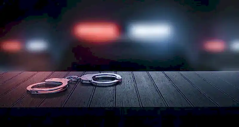 Loş ortamda masada duran kelepçe ve polis ışıkları – suç duyurusu süreci, şikayet dilekçesi ve hukuki başvuru yolları.