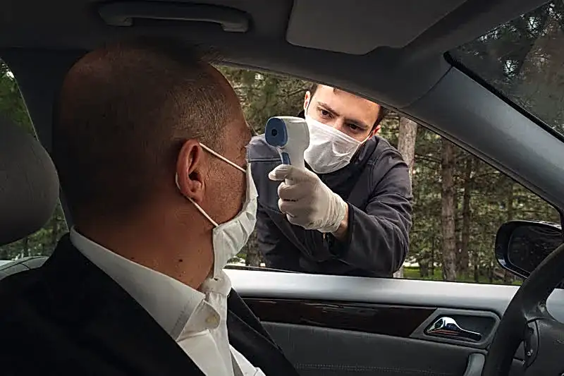 Trafik polisi, durdurduğu arabanın sürücüsünün ateşini ateş ölçer ile ölçüyor.