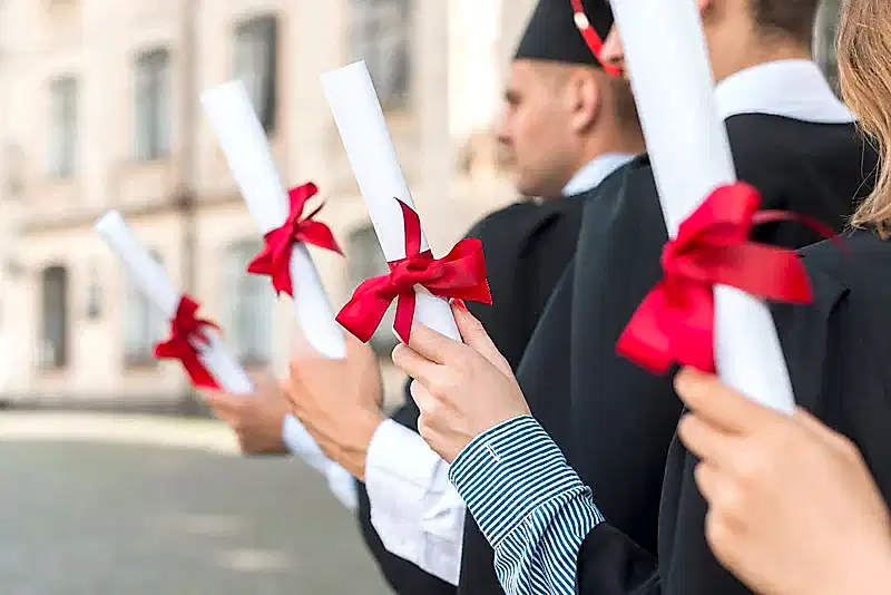 Sıraya dizilmiş 3 yeni mezun ellerinde diploma tutuyor.